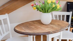 A round wooden table with a white vase of tulips, white chairs, and a wooden ceiling beam. - 1 bedroom accommodation in Ewelme (Ewelme)