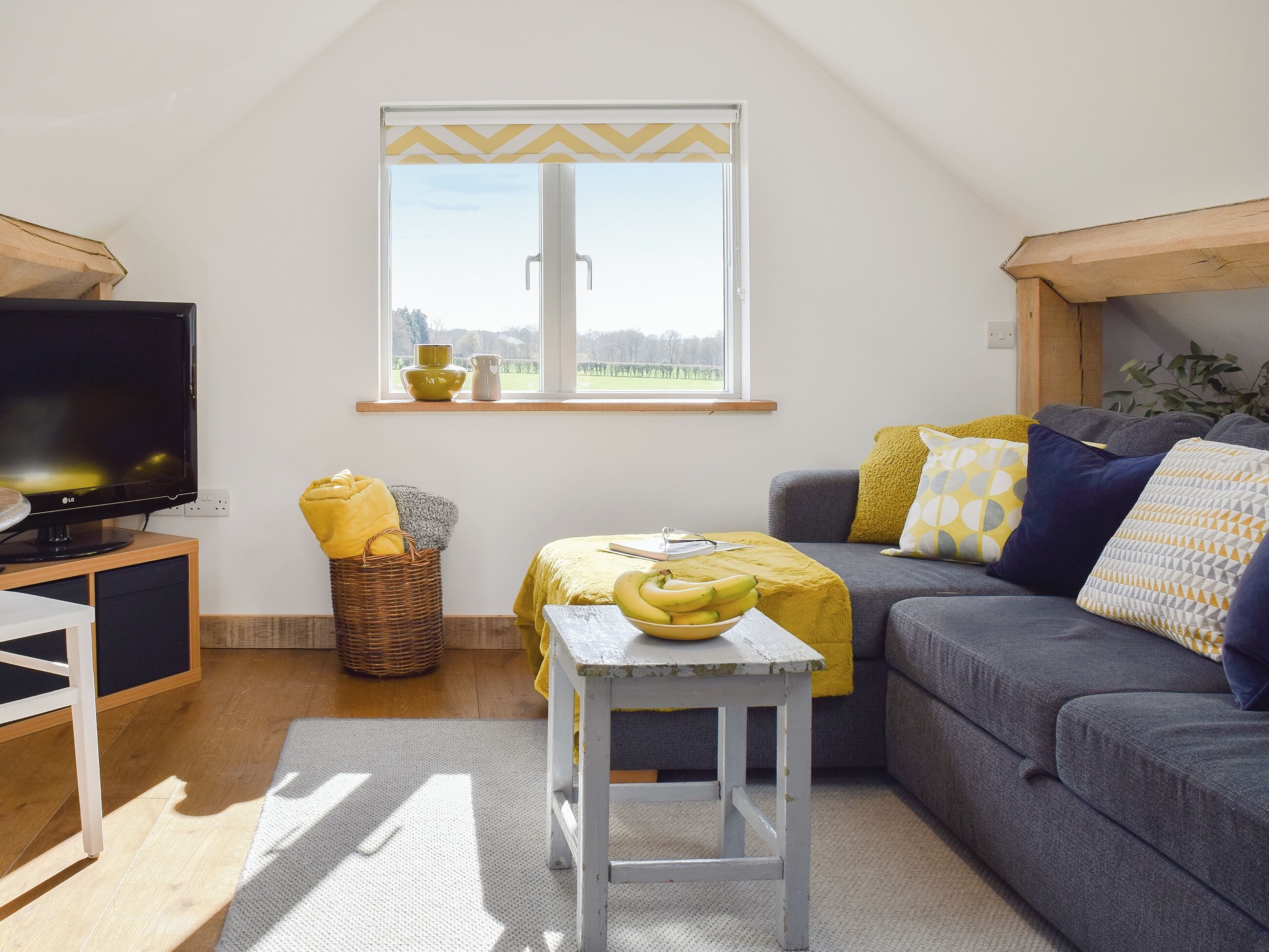 A living room with a television, a sofa, a small table, a window with a view, and a basket.