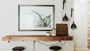 Un taulell de bar de fusta amb dos tamborets, una fotografia en blanc i negre emmarcada i dues làmpades pendents negres.