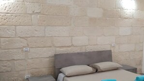 A bedroom with a stone wall, a bed with beige bedding, two pillows, and two folded towels on the bed. - Boffy Houses (Lecce)