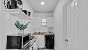A compact kitchen with white cabinetry, a microwave, a stove, a sink, and a small window. - Beach Studio · 2 Min Walk to Hollywood Broadwalk (Hollywood)