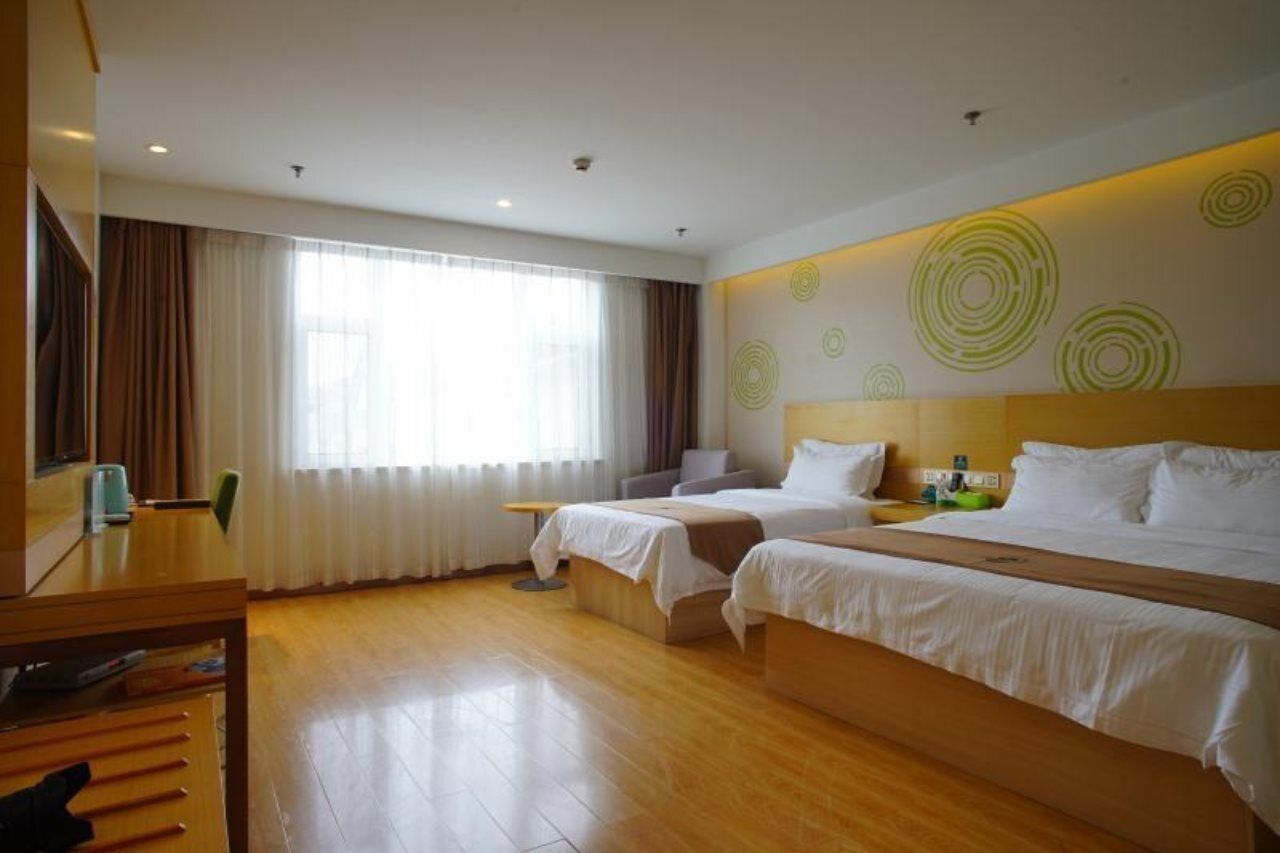 A hotel room with two beds, a wooden floor, a large window with curtains, and a wall with circular patterns.