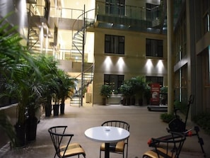 Un atrium à plusieurs niveaux, doté d’un escalier central, de plantes en pot et d’un espace extérieur aménagé pour s’asseoir.