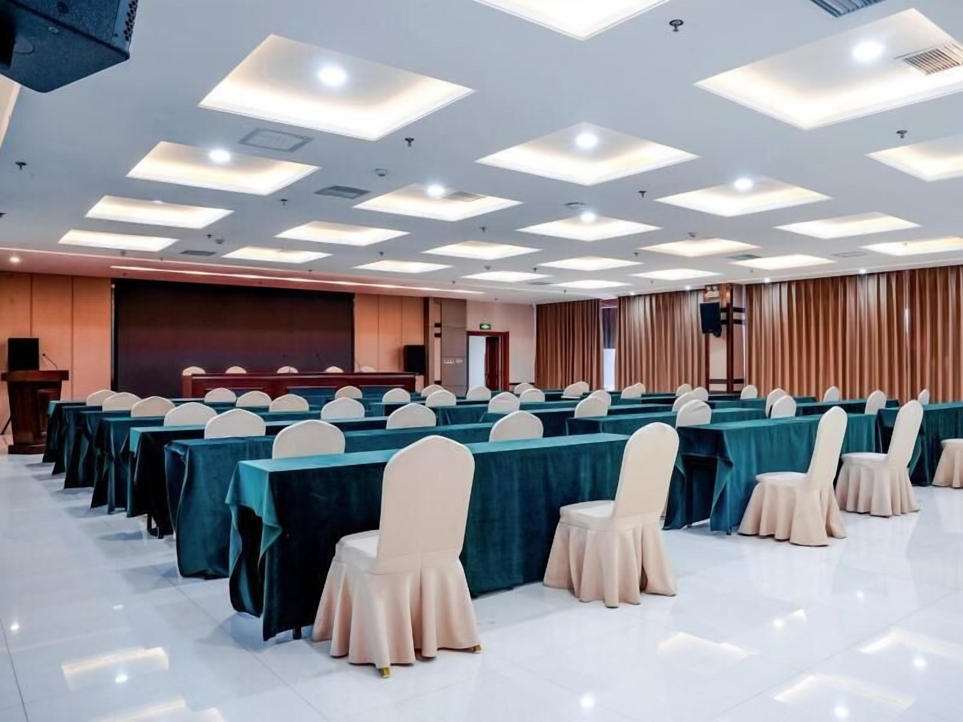 A conference room with rows of tables and chairs, a podium, and a large screen.