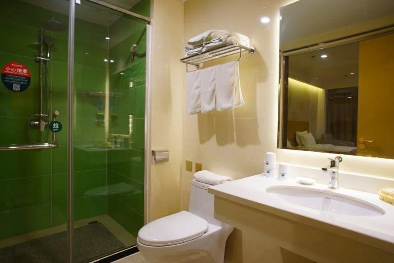 A bathroom with a glass-enclosed shower, a white toilet, a sink with a mirror, and a towel rack with folded towels.