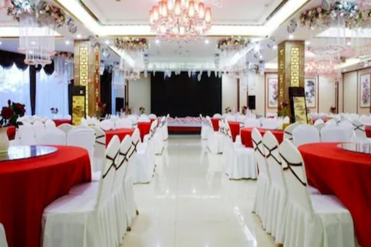 Un salón de banquetes con mesas redondas cubiertas con manteles rojos, sillas blancas y una araña.