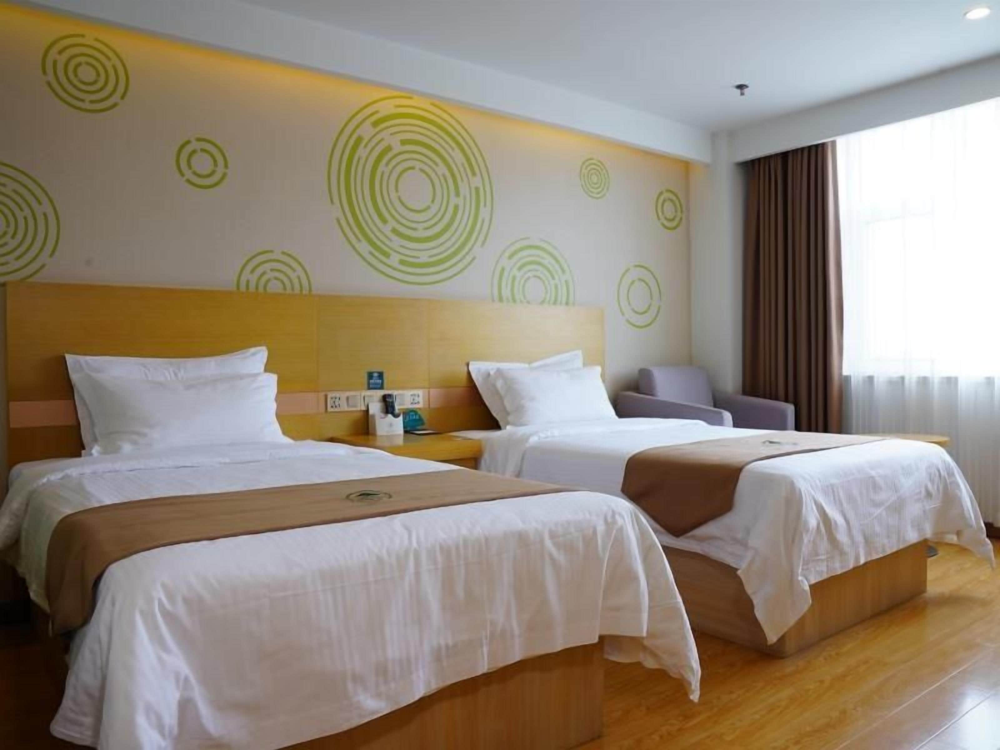 Quarto de hotel com duas camas, cabeceira de madeira, parede com desenhos circulares e janela com cortinas.