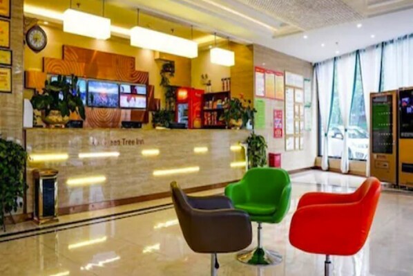 A hotel reception area with a marble counter, a clock, and a TV screen. There are three chairs in front of the counter.