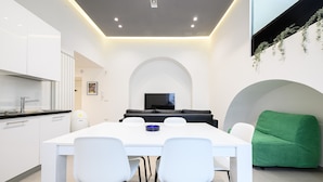 A modern kitchen with white cabinets and a black countertop, a dining area with a white table and chairs, a black sofa, and a green armchair.
