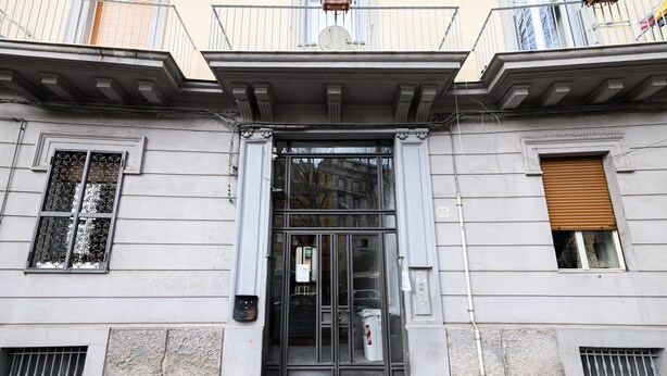 A building entrance with a glass door, a small window with a shutter, and a balcony with railings.