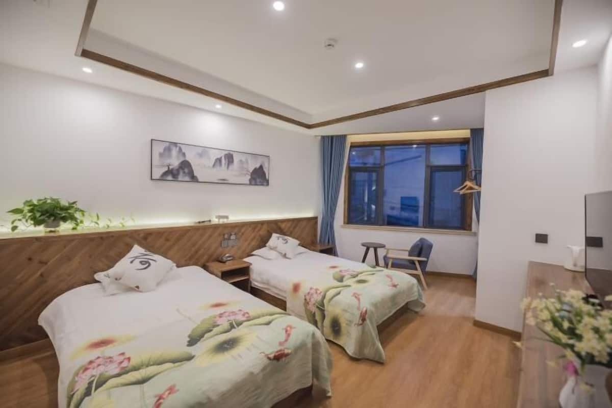 Two single beds with floral-patterned bedding and a wooden headboard, a desk, and a large window with an outside view.