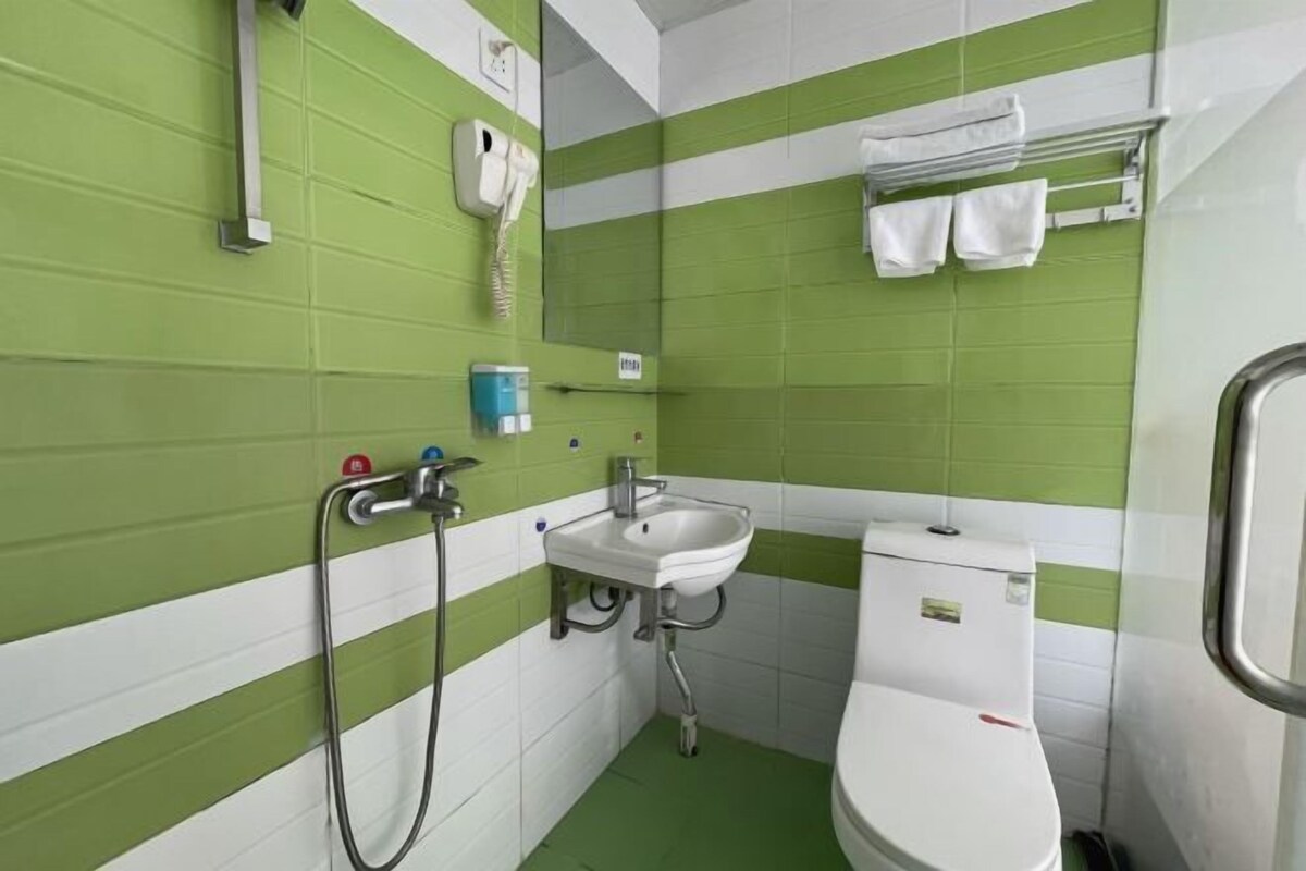 A small bathroom with green and white tiles, a white sink, a toilet, a shower, and a towel rack.
