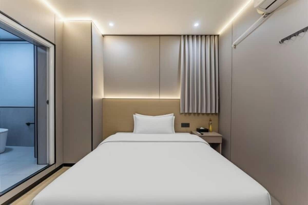 Une chambre d’hôtel moderne équipée d’un lit, d’une table de chevet, d’un miroir et d’une fenêtre avec des rideaux.