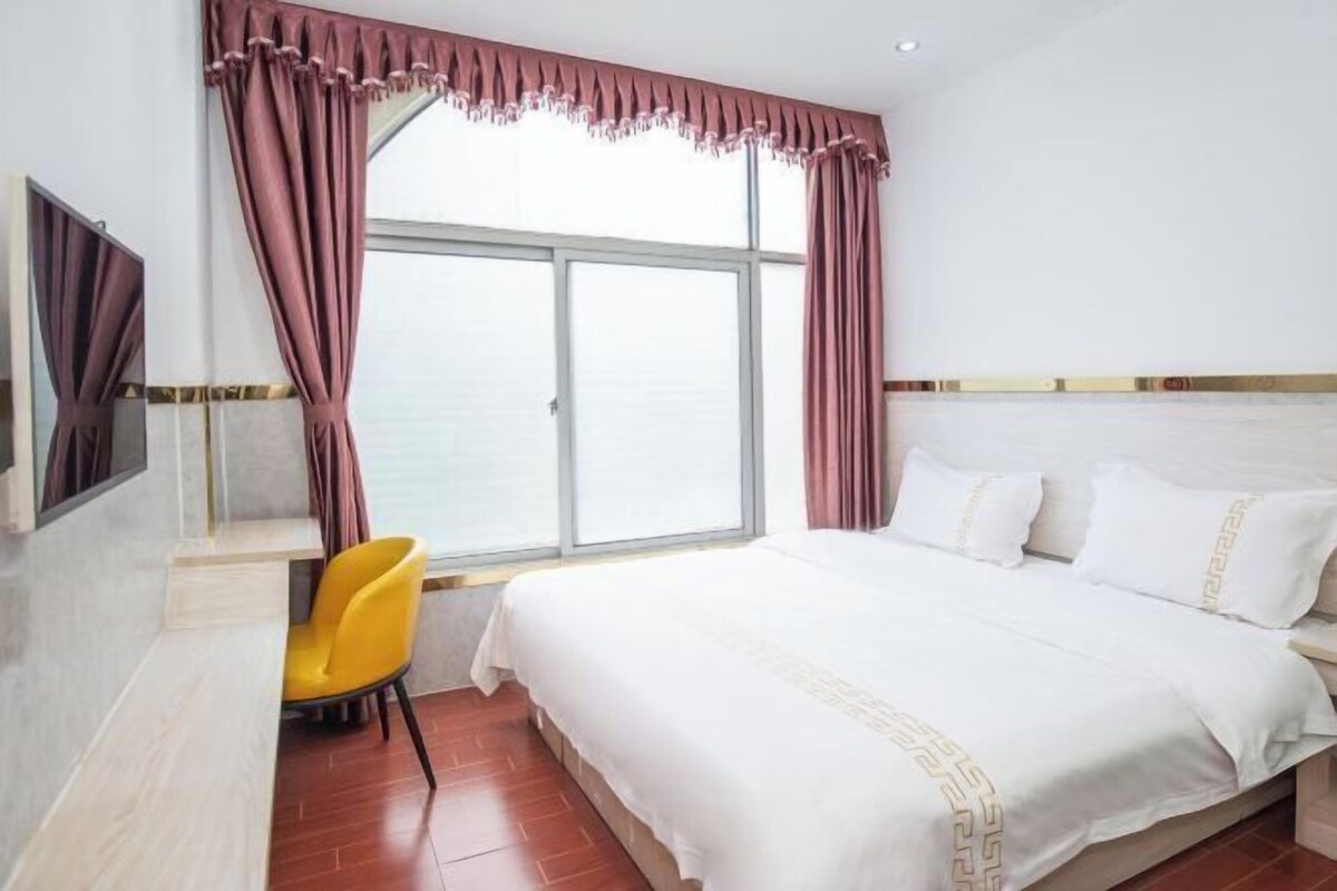 A hotel room with a large bed, a desk with a chair, a TV, and a window with curtains.