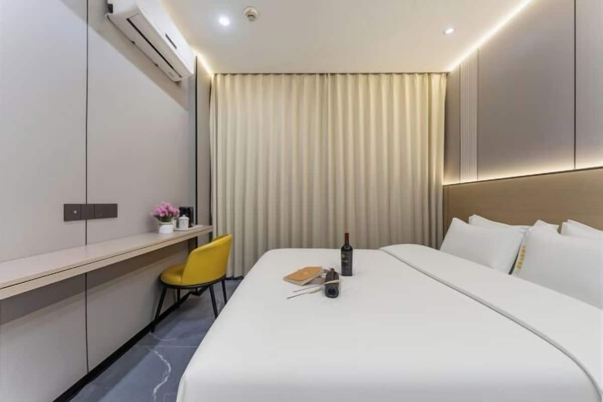 Une chambre d’hôtel moderne avec un lit bien fait, un bureau avec une chaise et une grande fenêtre avec des rideaux.