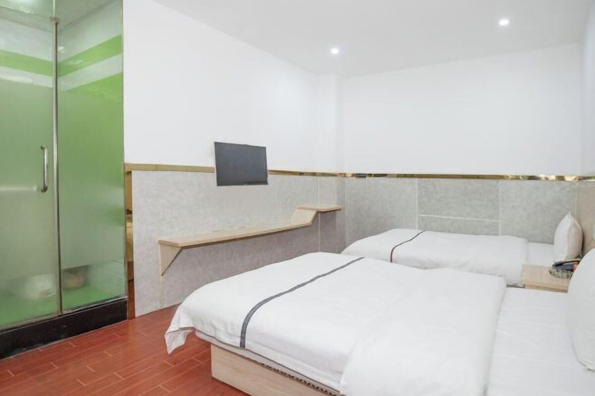 A hotel room with two beds, a TV mounted on the wall, and a glass shower enclosure.