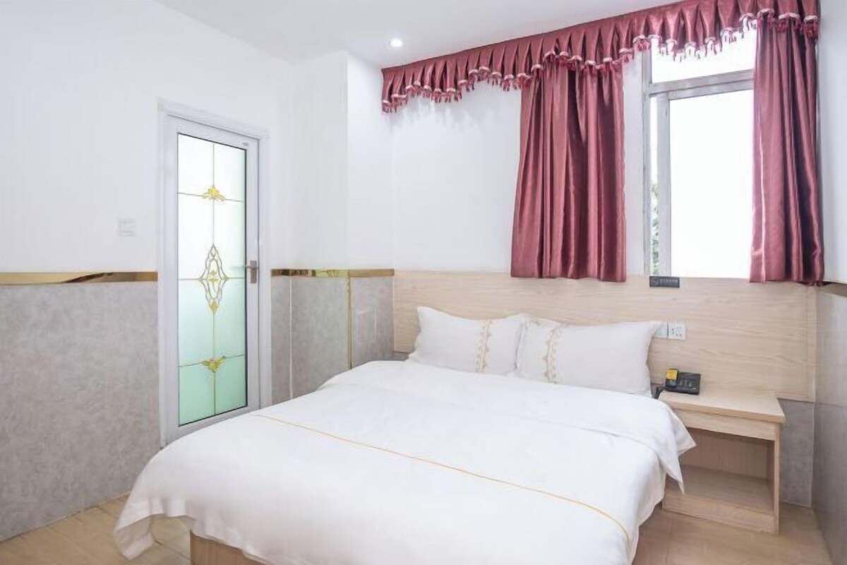 A bedroom with a bed, a bedside table, a nightstand, a window with curtains, and a door with a frosted glass panel.