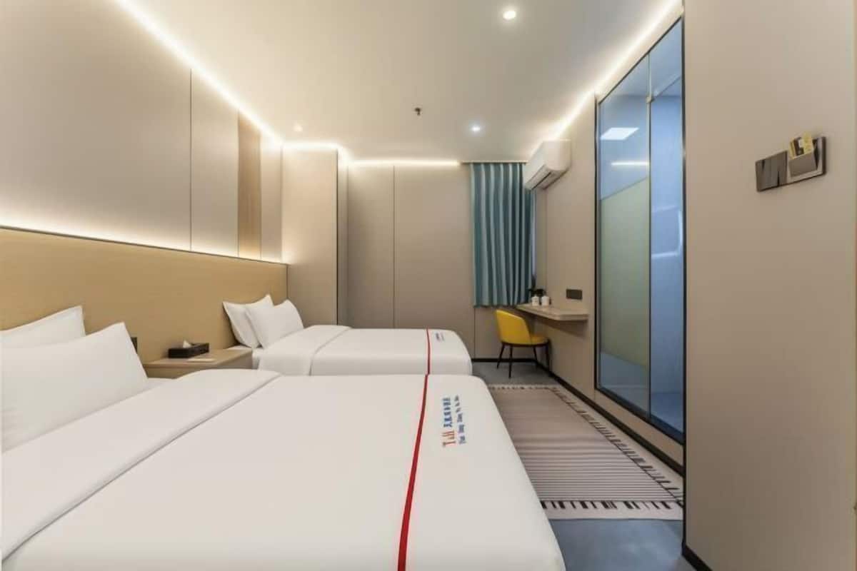 Une chambre d’hôtel avec deux lits, un bureau, une chaise, une fenêtre et un rideau.