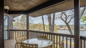 A covered outdoor seating area with a round table and chairs, overlooking a lake and trees. - South Shore Updated 2 Bdrm! Hot tub/Mini-Golf/Tennis/Pickleball & More! (Hot Springs)