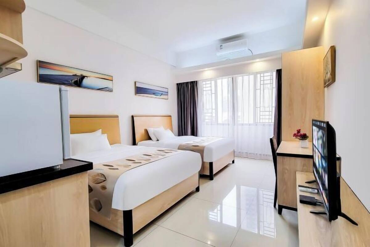 A hotel room with two beds, a desk with a TV, and artwork on the walls.