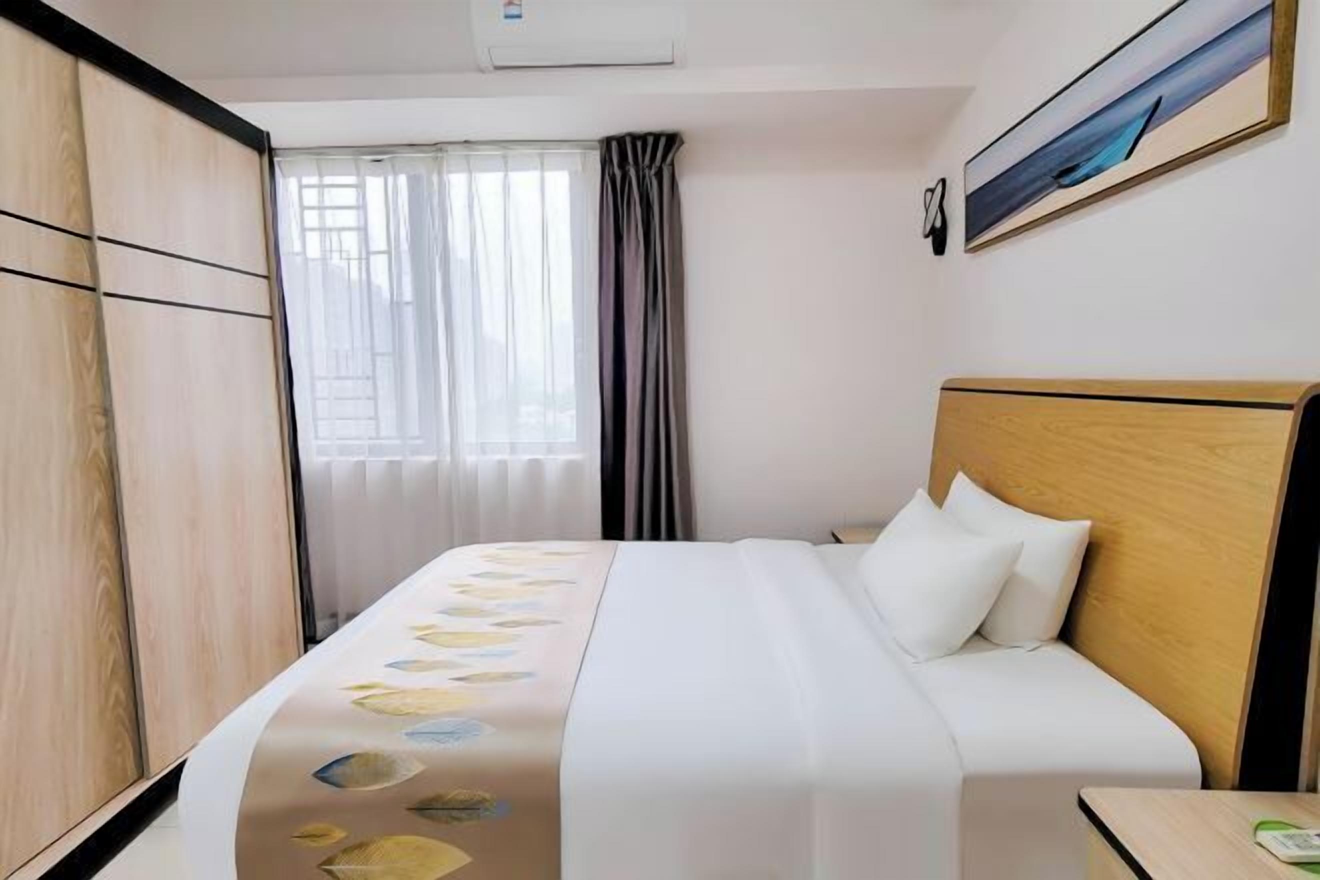 Una habitació d'hotel amb un llit, un panell de fusta al capçal, una finestra amb cortines i un quadre a la paret.