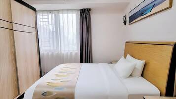 Una habitació d'hotel amb un llit, un panell de fusta al capçal, una finestra amb cortines i un quadre a la paret.