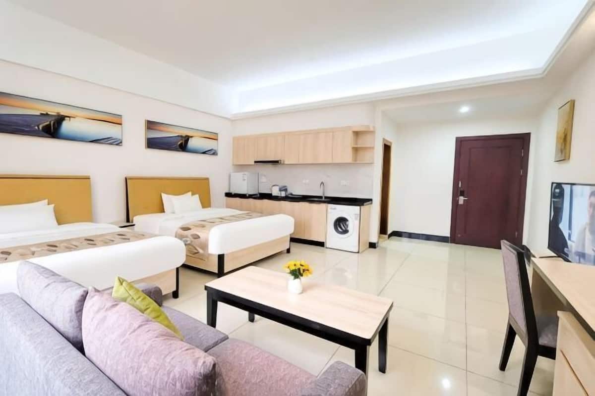 A modern hotel room with a sofa, a bed, a dining table, a kitchen area, and artwork on the walls.