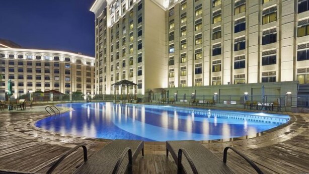 A hotel pool area with lounge chairs and a large building in the background. - Haili Apartment (Guangzhou)