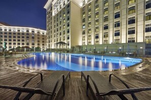 A hotel pool area with lounge chairs and a large building in the background. - Haili Apartment (Guangzhou)