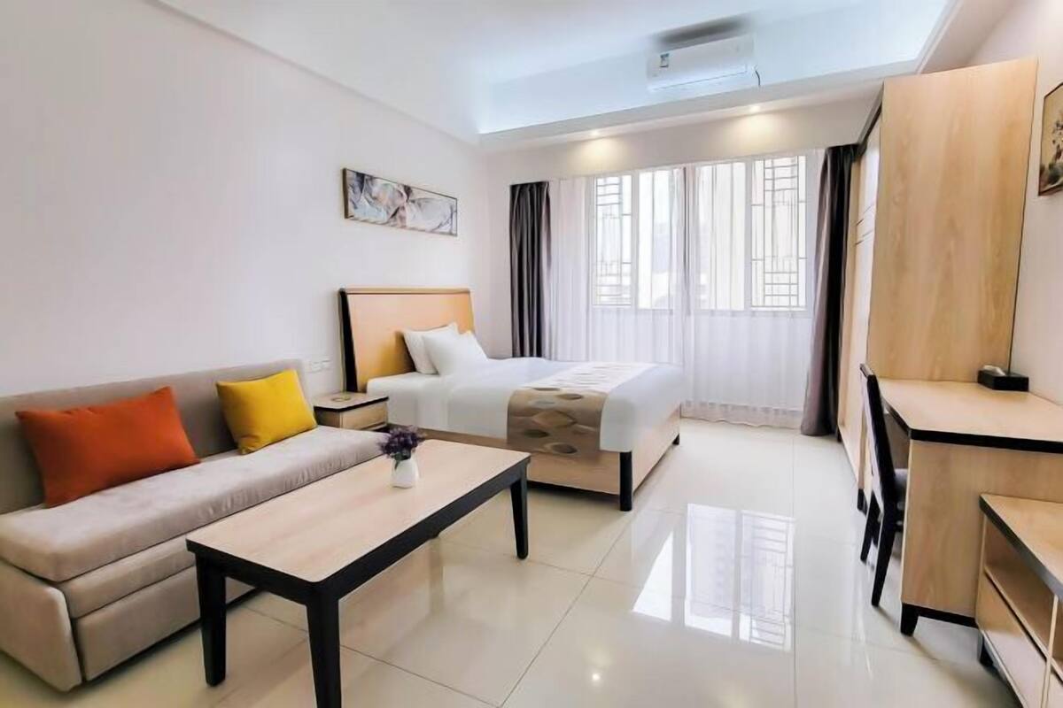 A modern hotel room with a bed, a sofa, a desk, and a window with curtains.