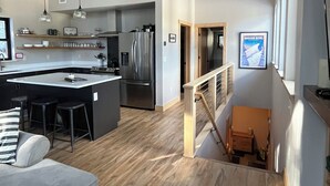 Een moderne keuken met een centraal eiland, een zithoek met een bank, en een trap naar een hoger gelegen verdieping.