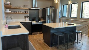 Een moderne keuken met een centraal eiland, roestvrijstalen apparatuur en barstoelen.