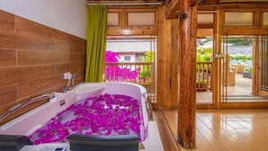 Ein Badezimmer mit einer Badewanne, gefüllt mit Rosenblättern, Holzwänden und einem Balkon mit Blick auf Grünflächen.