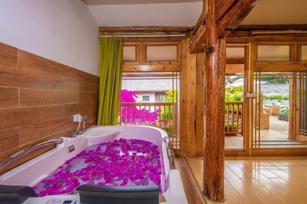 A bathroom with a bathtub filled with rose petals, wooden walls, and a balcony with a view of greenery. - Yuhuai Renjia Inn (Lijiang)