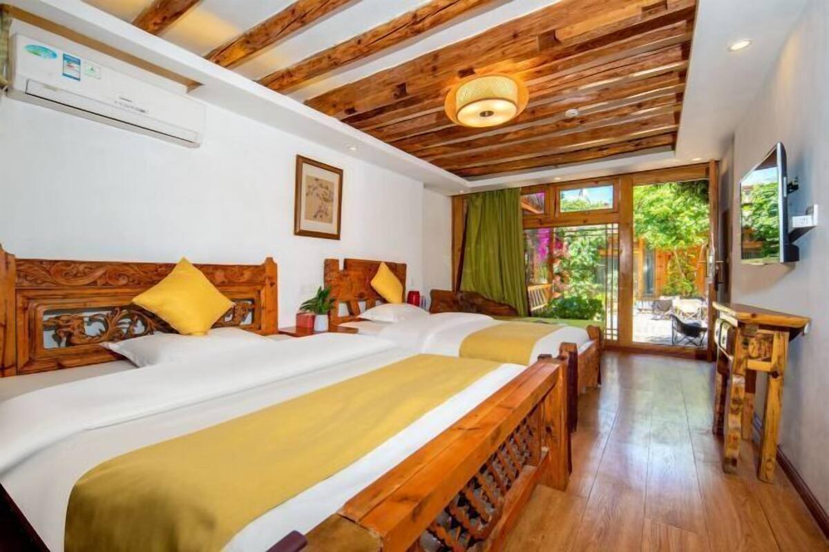 A hotel room with two beds, wooden headboards, a ceiling fan, a TV, and a window with a view of greenery.