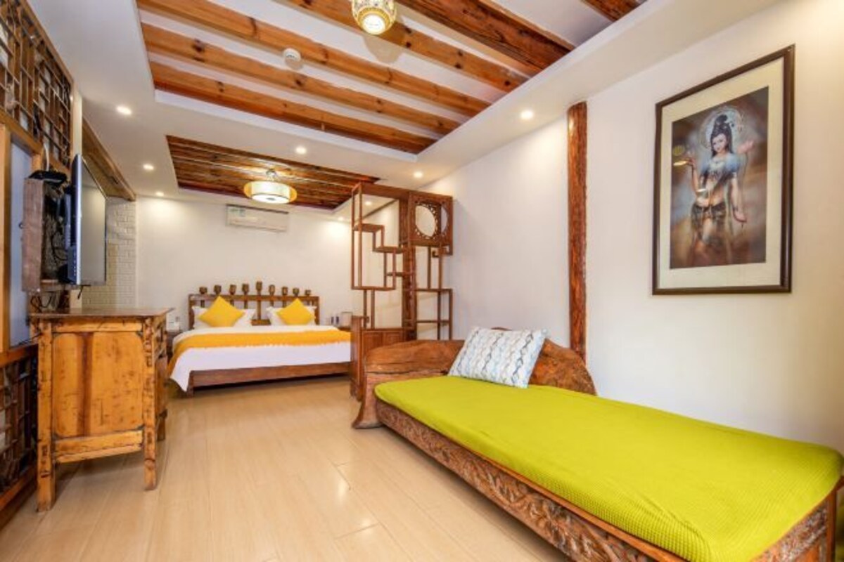 Una stanza con soffitto in legno, un letto con cuscini gialli, un divano verde e un quadro appeso al muro.