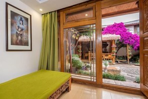 Una habitació amb un llit, una finestra amb vista a un jardí i un quadre al mur.