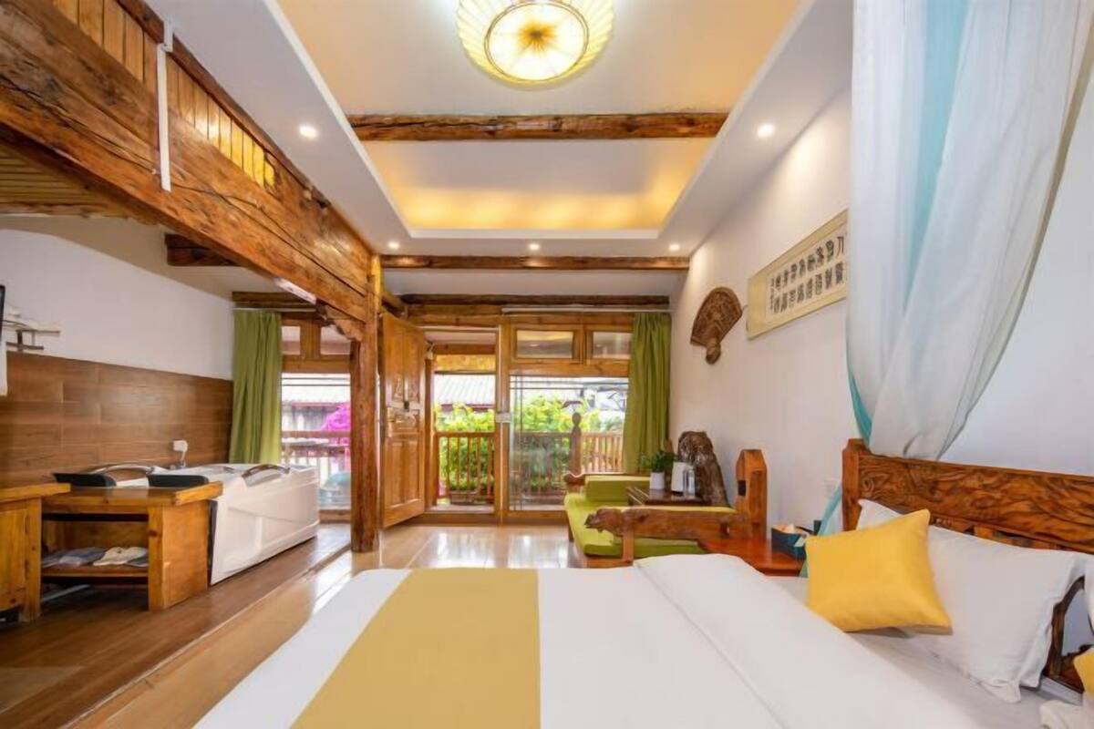 A hotel room with a wooden ceiling, a bed with white bedding, a wooden nightstand, and a view of greenery outside.
