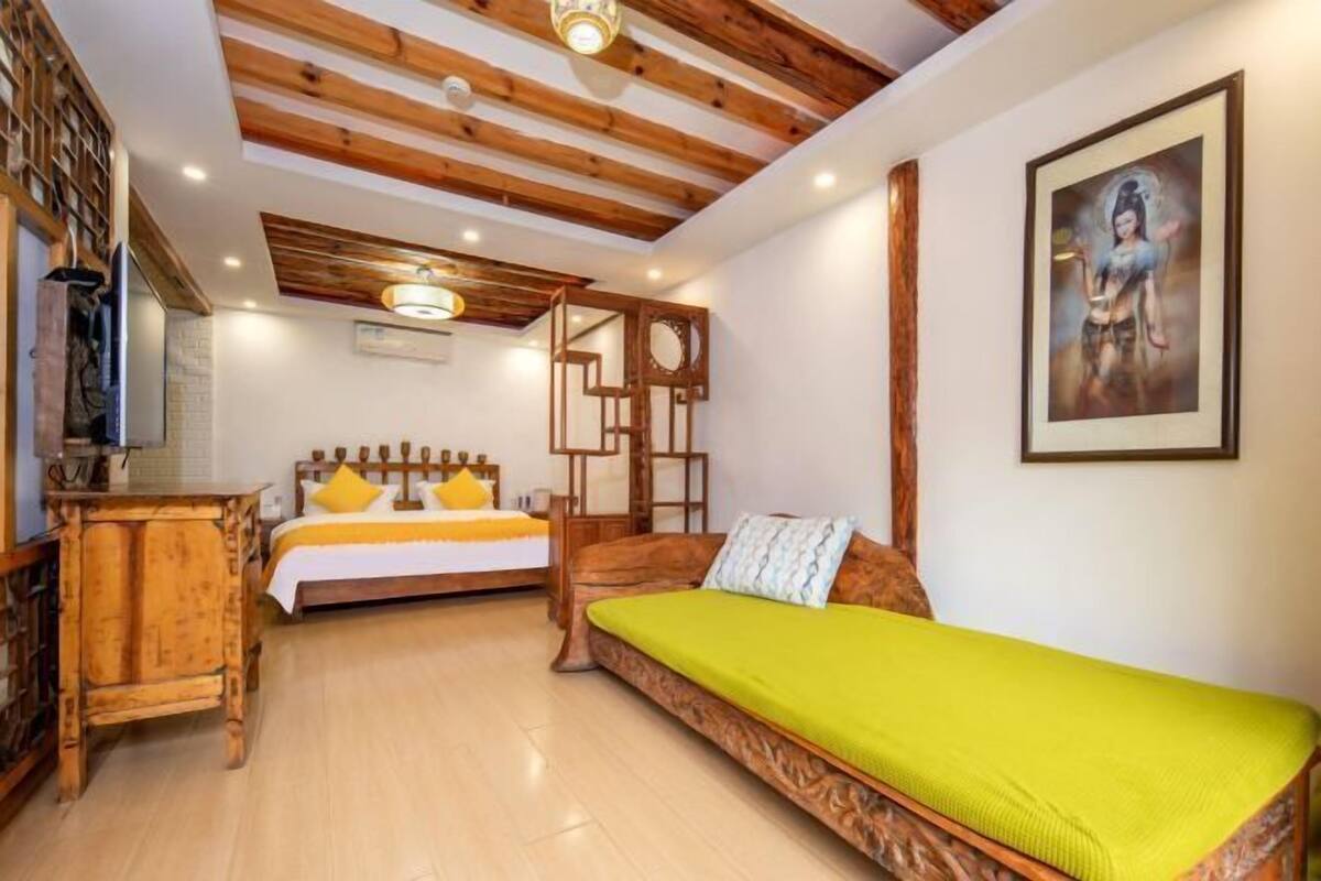 A room with a bed, a sofa, a wooden desk, and a painting on the wall.