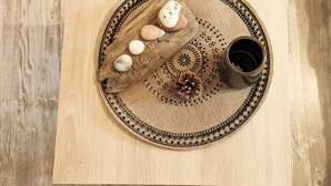 Une table en bois sur laquelle est posée une nappe en fibres tressées, une assiette avec des biscuits et une pomme de pin, ainsi qu’une tasse de café.