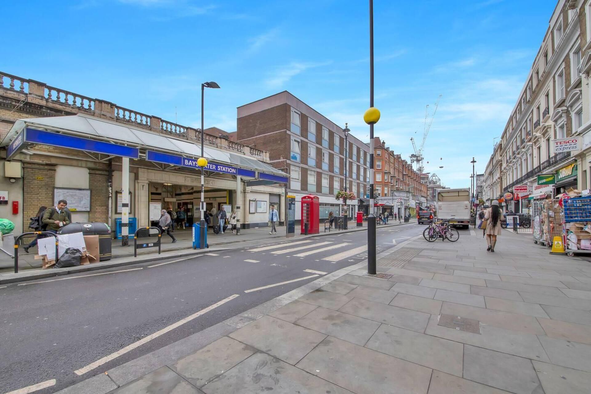 Une vue de rue avec l’entrée d’une gare, des commerces et un passage piéton.