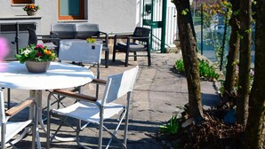 An outdoor seating area with a table and chairs, a potted plant, and a view of a building with windows and a door. - Quadrifoglio by Wonderful Italy (Bellagio)