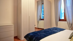 A bedroom with a bed, a wardrobe, and a window with curtains. - Quadrifoglio by Wonderful Italy (Bellagio)