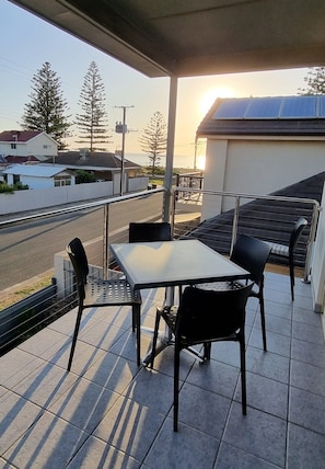 A balcony with a table and chairs, overlooking a street and houses. - Sandrift by the beach (Largs North)
