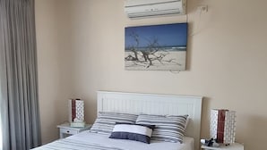 A bedroom with a bed, a nightstand, a wall-mounted air conditioner, and a painting. - Sandrift by the beach (Largs North)