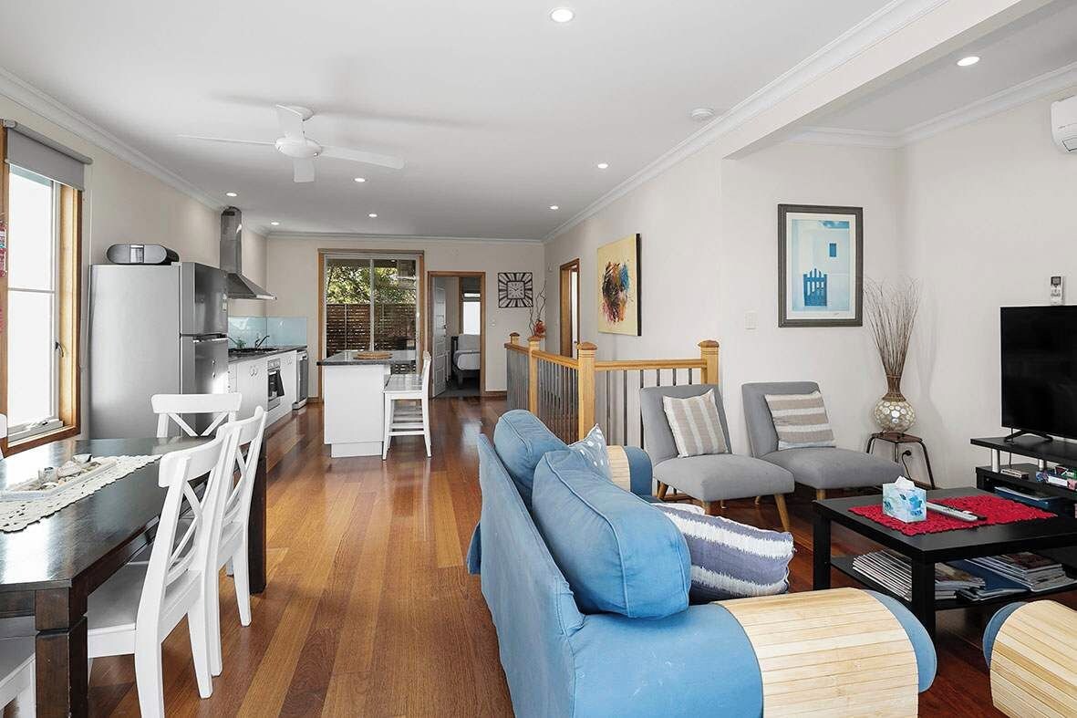 A modern living room with a sofa, chairs, a dining table, and a kitchen in the background.