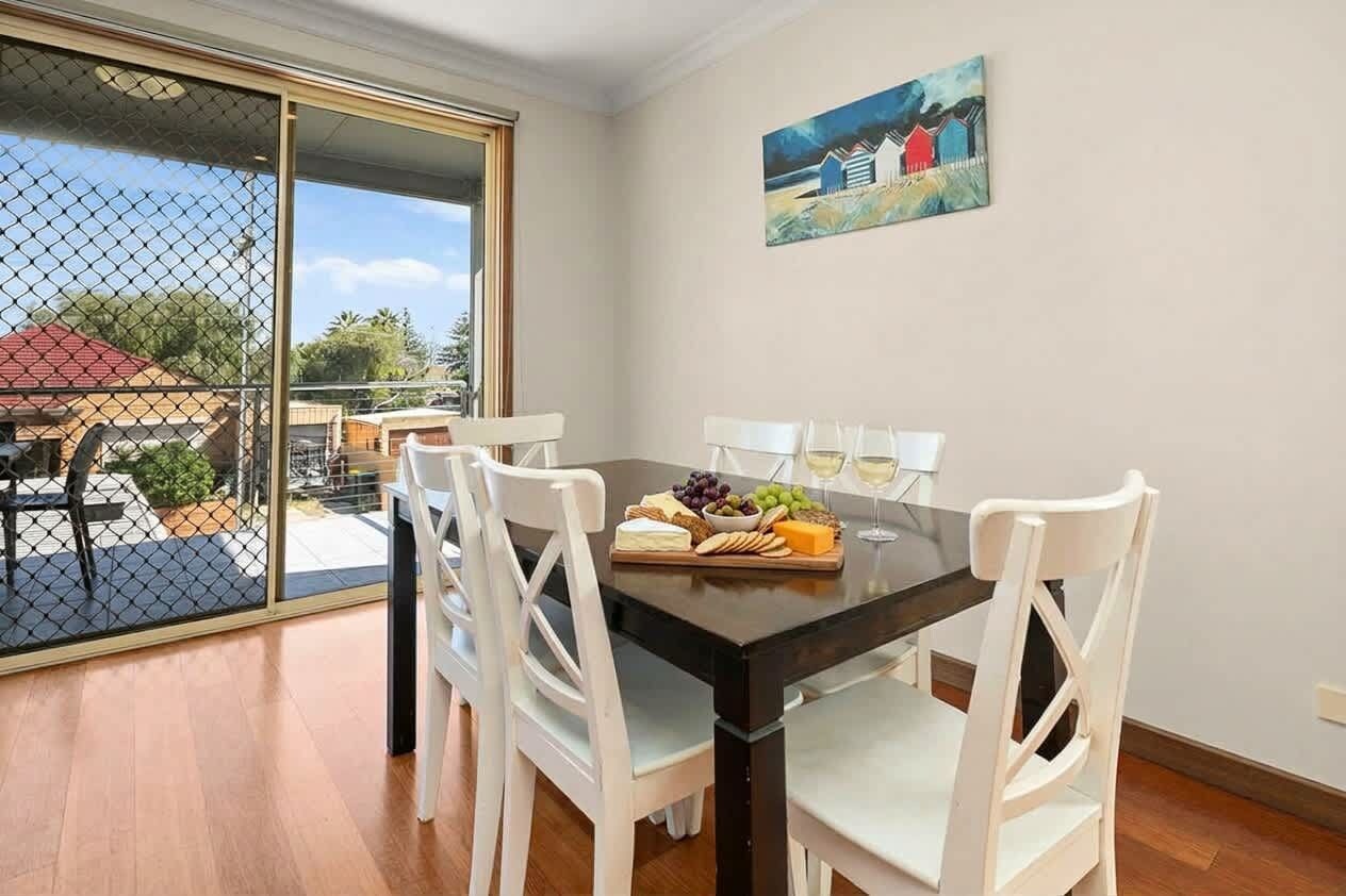 Un coin repas avec une table dressée pour quatre personnes, un tableau accroché au mur et une vue à travers une porte vitrée.