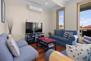 A living room with a flat-screen TV, a blue sofa, and a coffee table. - Sandrift by the beach (Largs North)
