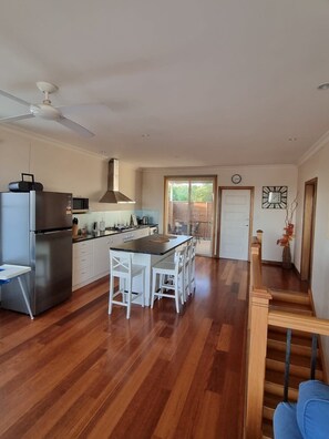 A modern kitchen with a central island, white cabinetry, and a stainless steel refrigerator. - Sandrift by the beach (Largs North)