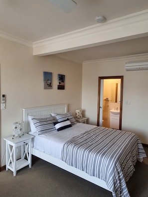 A bedroom with a white bed, striped bedding, a nightstand, and a small table with decorative items. - Sandrift by the beach (Largs North)